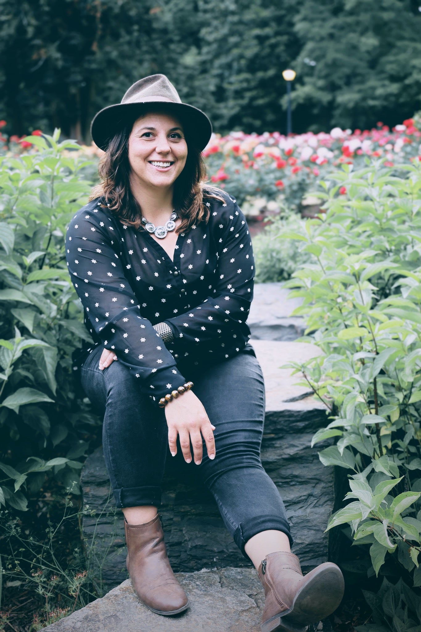 Woman sitting on a stone path in a garden with flowers and greenery. Small batch holistic traditional Chinese medicine and southern folk craft in Durham, NC. Kimberly Foytlin-Zhang. Owner of Pine and Pangolin.