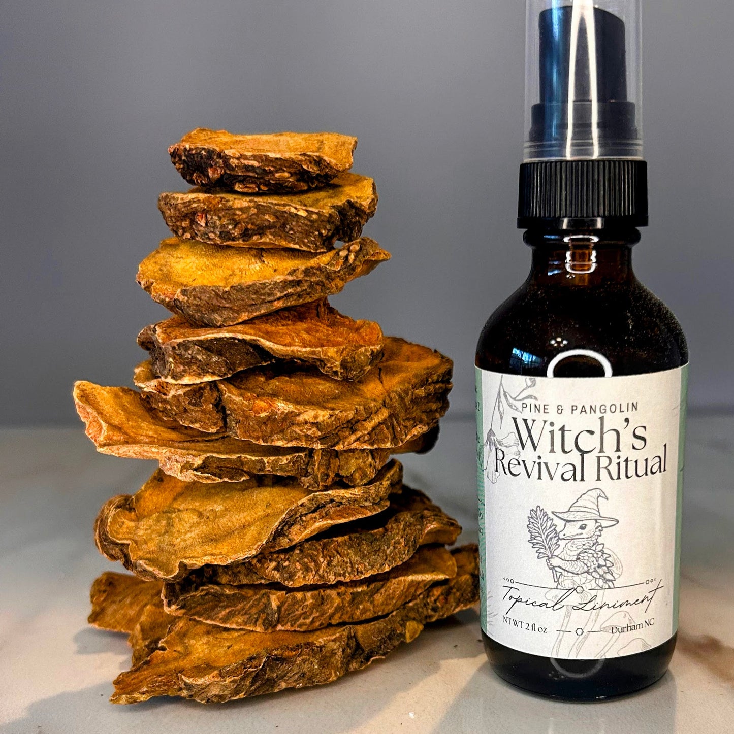 Bottle of 'Witch's Revival Ritual' on a marble surface with stacked wooden pieces. Small batch holistic traditional Chinese medicine and southern folk craft in Durham, NC.