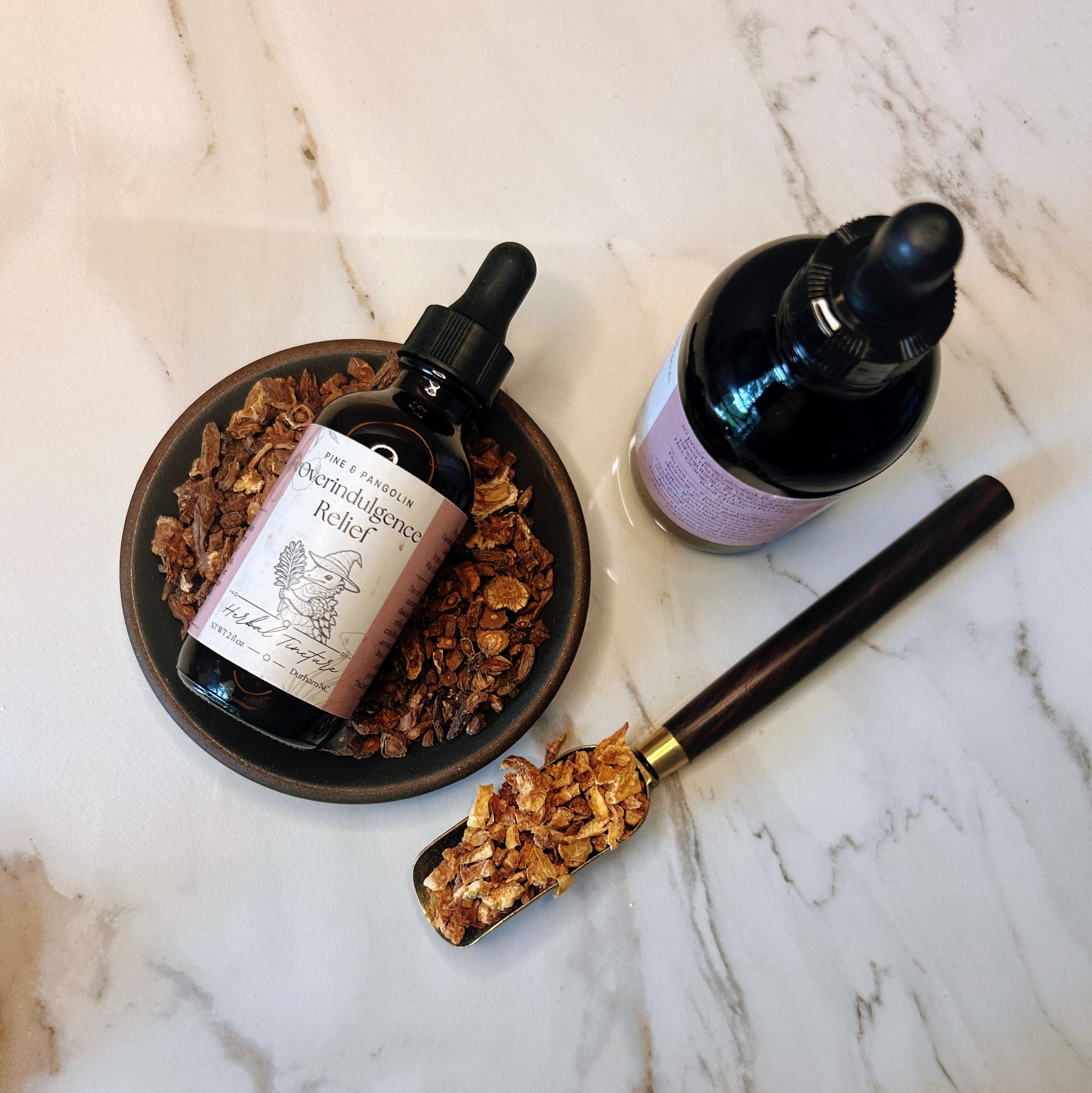 Two bottles of 'Indulgence Relief' on a marble surface with a scoop of granola. Tincture. Durham, NC