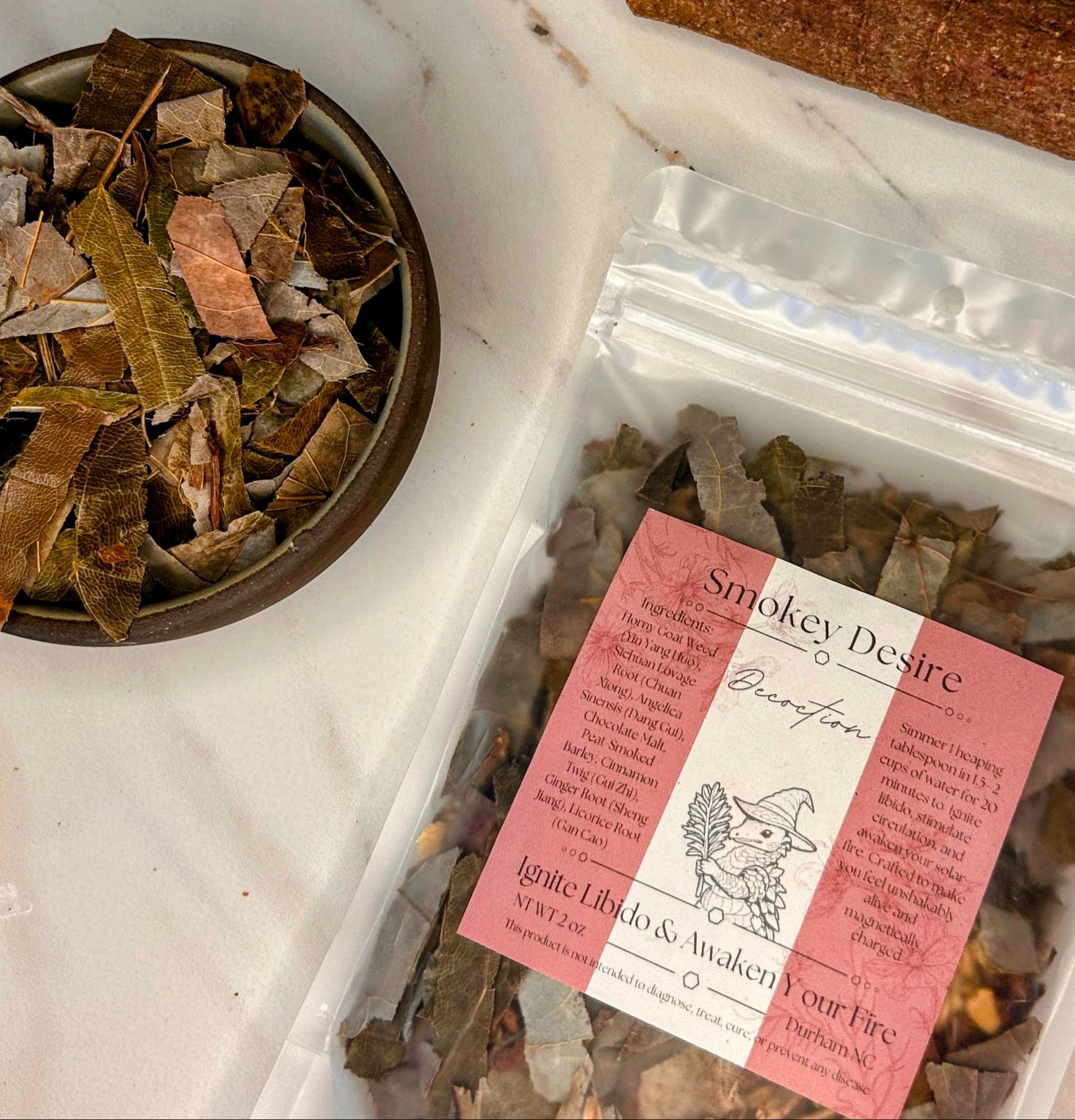 Herbal products including a bowl of dried leaves, a package labeled 'Smokey Desire', and a card on a white surface. Small batch holistic traditional Chinese medicine and southern folk craft in Durham, NC. 