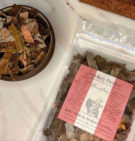 Herbal products including a bowl of dried leaves, a package labeled 'Smokey Desire', and a card on a white surface. Small batch holistic traditional Chinese medicine and southern folk craft in Durham, NC. 