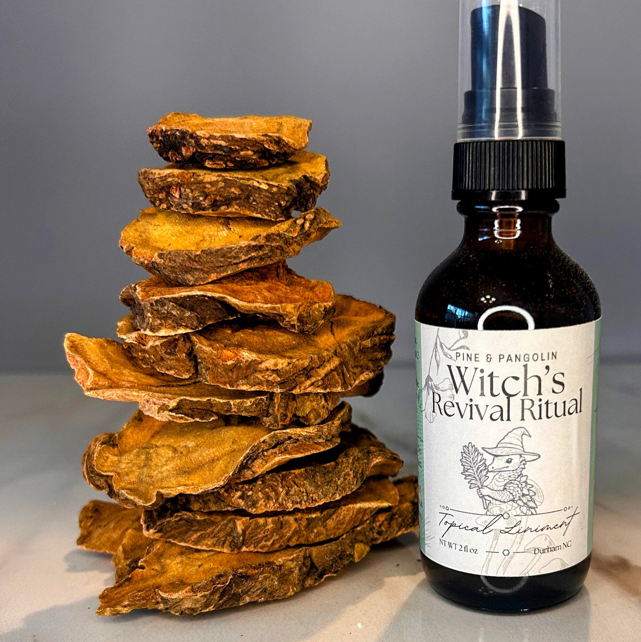 Bottle of 'Witch's Revival Ritual' on a marble surface with stacked wooden pieces. Small batch holistic traditional Chinese medicine and southern folk craft in Durham, NC. 